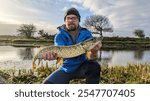 Man holding Northern pike freshwater fish caught in Cregg river, Galway, Ireland, water animals and wildlife, nature background, fishing, catch and release	