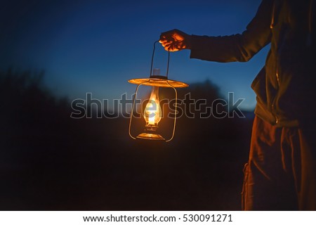 man holding the old lamp with a candle outdoors. hand holds a large lamp in the dark. ancient lantern with a candle illuminates the way on a night