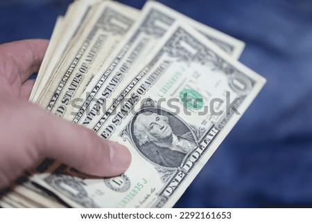 A man holding one dollar bills. Blue background.
