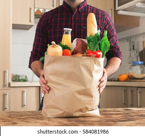 Man holding a paper bag full of healthy food on a wooden table in the home kitchen