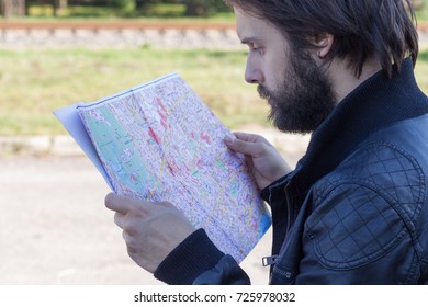 Man Holding A Paper Map In His Hands. Searching For Something In The Map.