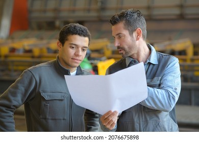 Man Holding Paperwork And Giving Instructions To Junior Worker