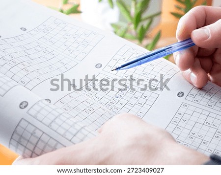 Man holding pen and solving difficult sudoku logical puzzle in paper book at home