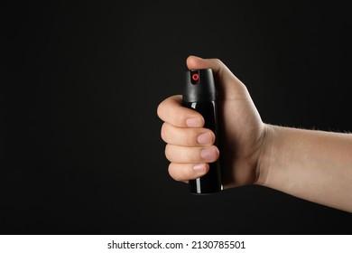 Man holding pepper spray on black background, closeup. Space for text