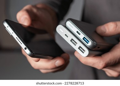 the man is holding the phone and the charger. Powerbank and smartphone in hand. Power-saving device power bank smartphone