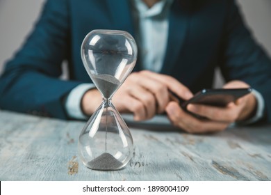 man holding phone with hourglass on table
