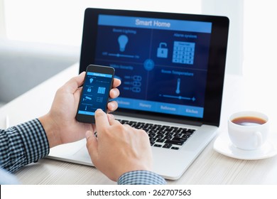 man holding the phone with program smart home on the screen against the background of the computer