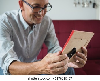 Man Holding A Photo Frame Sitting On Red Couch With Blurred Background         