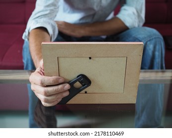 Man Holding A Photo Frame Sitting On Red Couch With Blurred Background         