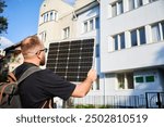 Man holding photovoltaic solar panel in front of historical building. Concept of integration of sustainable renewable energy sources into architecture.