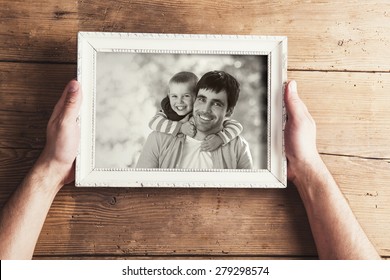 Man Holding A Picture Frame With Family Photo On A Wooden Background.