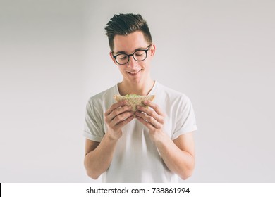 man holding a piece of hamburger. student eats fast food. not helpful food. very hungry man. Nerd is wearing glasses.