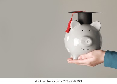 Man holding piggy bank and graduation cap against grey background, closeup with space for text. Scholarship concept