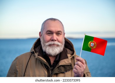 Man holding Portugal flag. 
Portrait of older man with a national Portuguese flag. 
Visit Portugal concept. Older man 50 55 60 years old 
with gray beard outdoors travelling in winter. Travel Portugal - Shutterstock ID 2233373395
