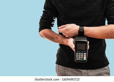 Man Holding Pos Terminal And Using Smartwatch To Pay. Concept Of NFC Technology, Cashless Or Contactless Payment. Person Isolated On Blue Background With Copy Space