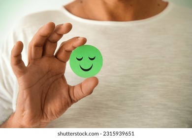 Man holding a positive green emoji. Smile, satisfaction. Copy space.