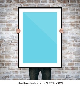 Man Holding Poster Mockup With Frame On Brick Background