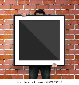 Man Holding Poster Mockup Template With Black Frame On Brick Bac