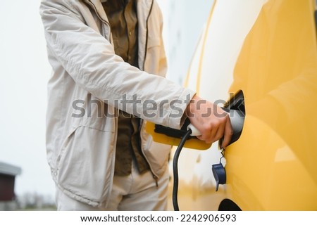 Man Holding Power Charging Cable For Electric Car In Outdoor Car Park. And he s going to connect the car to the charging station in the parking lot near the shopping center. Foto stock © 