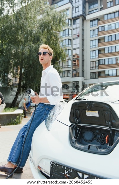 Man Holding Power\
Charging Cable For Electric Car In Outdoor Car Park. And he s going\
to connect the car to the charging station in the parking lot near\
the shopping center