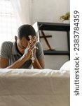 Man holding and praying rosary over a bed at home interior. Christian life concept.