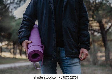 Man holding a purple yoga mat in a park wearing blue jeans. Exercise in nature outdoors concept - Powered by Shutterstock