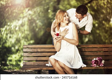 Man Holding Red Box With Ring Making Propose To His Girlfriend Outdoors.