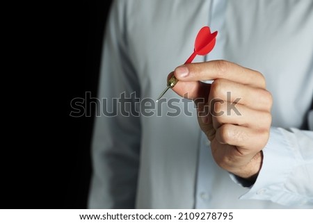 Man holding red dart on black background, closeup. Space for text