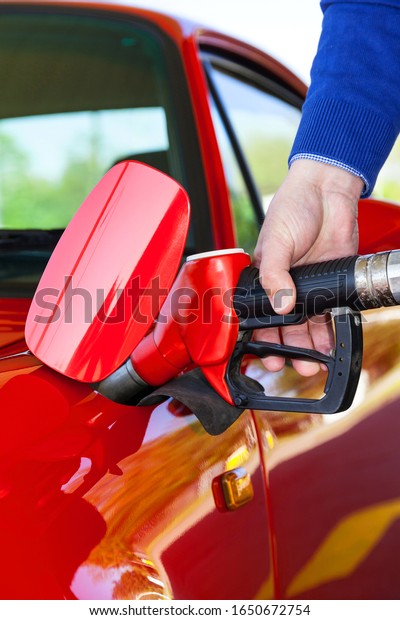 Man\
holding red fuel gun while refueling a red\
sportscar.