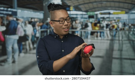 Man holding a red game controller and tapping buttons while checking it at an airport check in queue; travel curiosity.