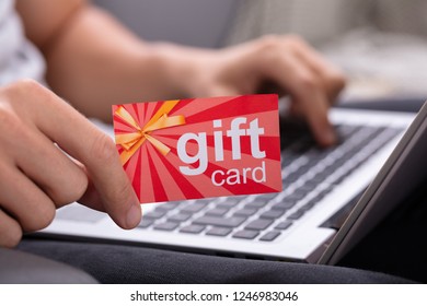 Man Holding Red Gift Card While Typing On Laptop Keypad