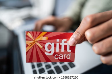 Man Holding Red Gift Card While Typing On Laptop Keypad