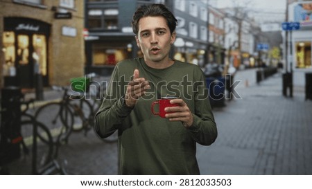 Man holding red mug and gesturing with left hand on a city street with bicycles and shopfronts; quiet contemplation.