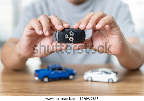 Man\
holding remote control of car for lock and Un-lock car In the\
anti-theft system and model toy a car on wood\
floor