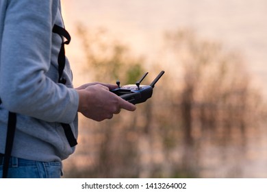Man holding remote control and navigating small drone with blurred sunset light in the background. Selective focus, blurred background. New technology, devices, gadgets concept.