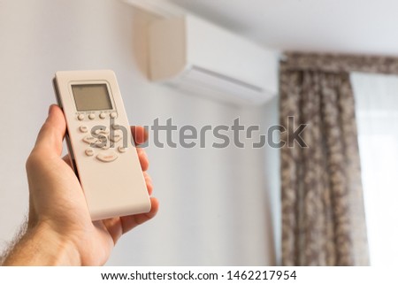 The man is holding a remote control from the non-working air conditioner. Hot in the room. Climate control in the apartment
