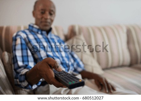 Man holding remote control while sitting on sofa in living room at home