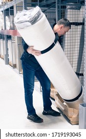 Man Holding Roll Of Mattress In Warehouse