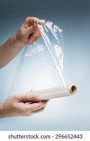 Man Holding A Roll Of Plastic Film, Typically Used For Sealing Food Items.