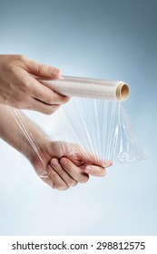 Man Holding A Roll Of Plastic Film, Typically Used For Sealing Food Items.