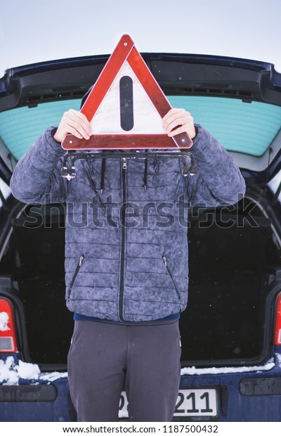 Man holding safety car triangle near head in  front\
of his damaged car.