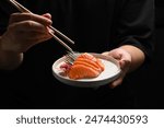 Man holding salmon sashimi with chopsticks on black background. Japanese food style concept