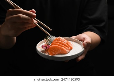 Man holding salmon sashimi with chopsticks on black background. Japanese food style concept - Powered by Shutterstock