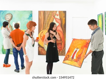 Man Holding And Showing A Colorful Painting To Other People In An Art Gallery