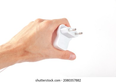 Man Holding A Simple White Wired Phone Charger, EU Plug, Generic Smartphone Charger Held In Hand Isolated On White, Cut Out. Consumer Electronics Industry, Charging Mobile Devices Concept, Technology