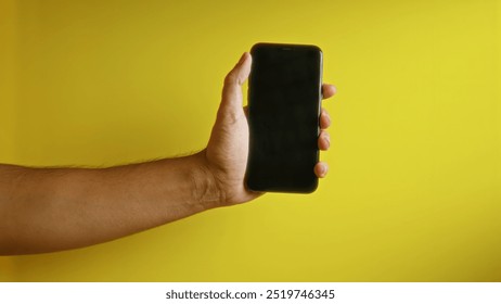 Man holding smartphone with black screen against vibrant yellow background creating a modern and minimalistic scene - Powered by Shutterstock