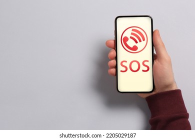 Man Holding Smartphone With Emergency Call SOS On Screen On Light Grey Background, Space For Text