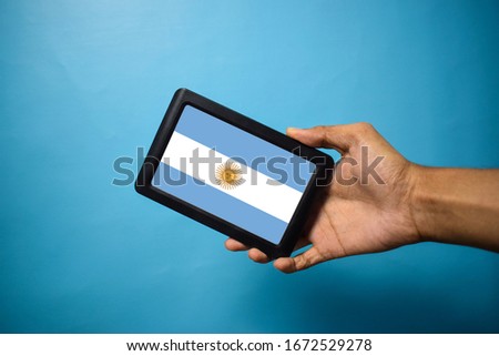 Man holding Smartphone with Flag of Argentina. Argentina Flag on Mobile Screen isolated On Blue Background