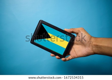 Man holding Smartphone with Flag of Bahama . Bahama Flag on Mobile Screen isolated On Blue Background
