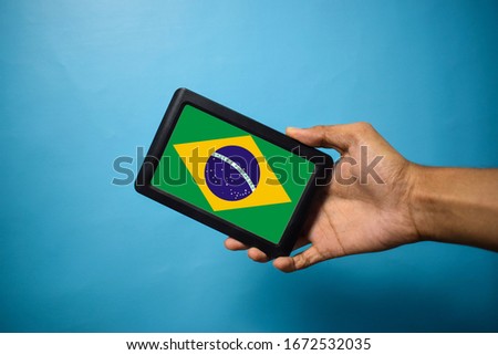 Man holding Smartphone with Flag of Brazil. Brazil Flag on Mobile Screen isolated On Blue Background